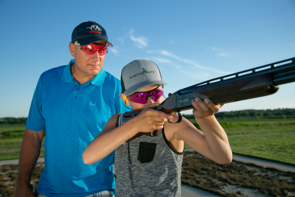 A male shooting instructor teaching a boy on the trap range.