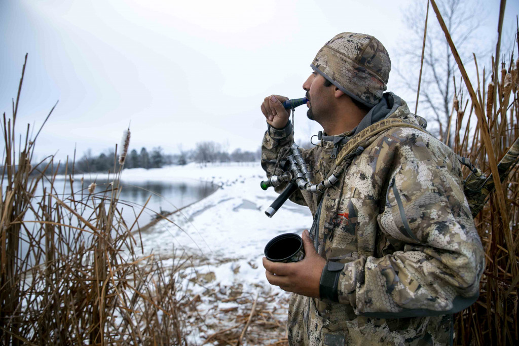 A man calling in ducks while hunting in the snow.