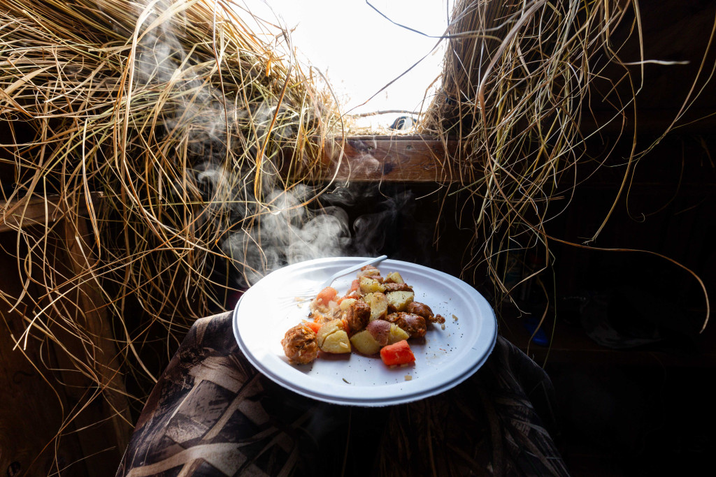 A plate of potatoes and sausages steams in the cold air in a goose blind