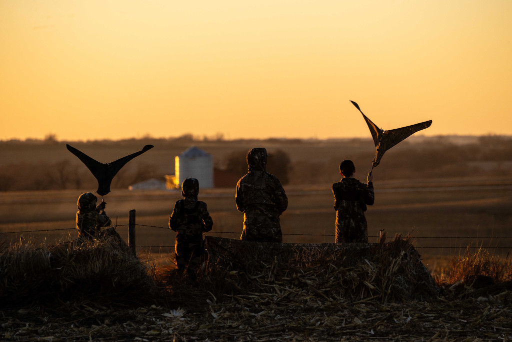 four hunters wave flags; they are silhouetted against a yellowing sky 