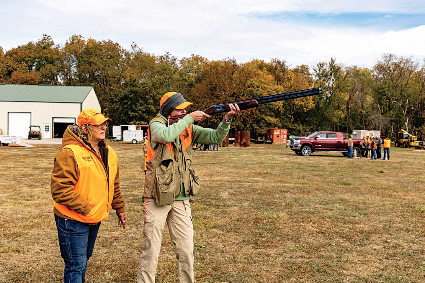 A female mentor teaching a younger woman how to shoot clay targets.