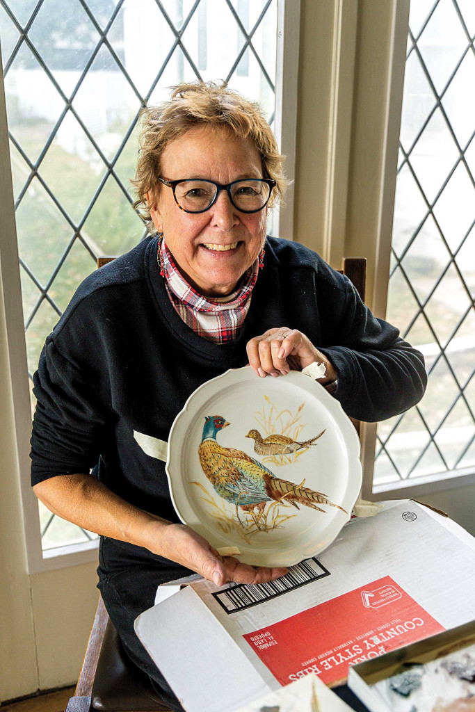 A woman who holding a plate where she painted a couple pheasants.