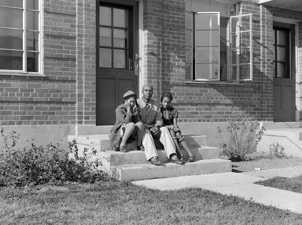 Three African Americans sit on a front porch of public housing during the Great Depression in Omaha, Nebraska