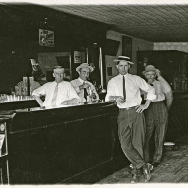 Men line up behind the bar and in front of it with smug smiles for a photograph