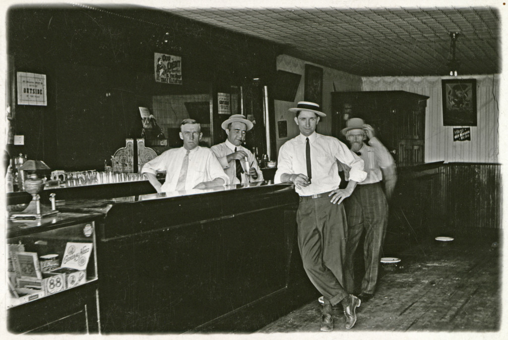 Men line up behind the bar and in front of it with smug smiles for a photograph