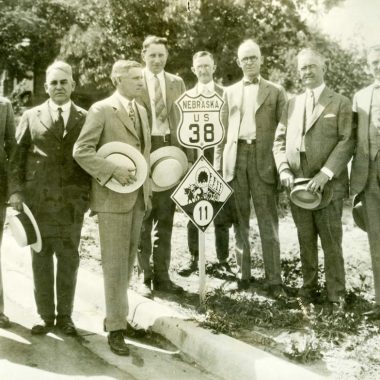 Men in suits pose next to a newly installed highway marker for U.S. Highway 38 through Nebraska