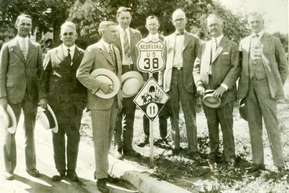 Men in suits pose next to a newly installed highway marker for U.S. Highway 38 through Nebraska