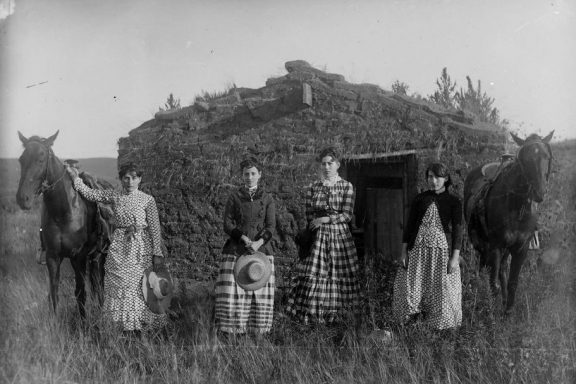 Four sisters pose in front of a sod house on the Nebraska prairie in 1886.