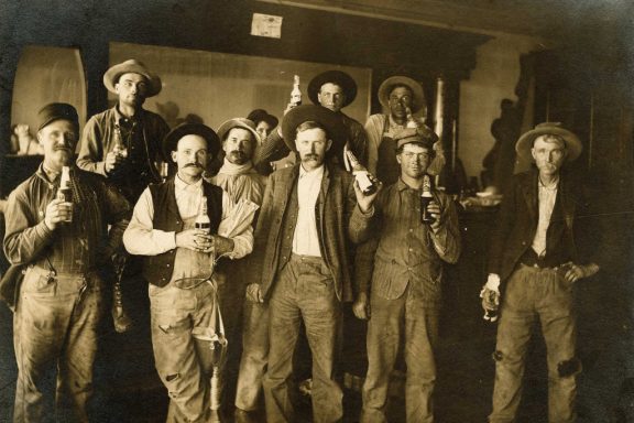 Men pose for the camera with their beer bottles during the Prohibition era in this sepia-toned photo