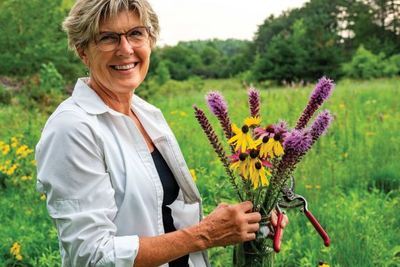 A woman poses in her backyard, which she restored into prairie.