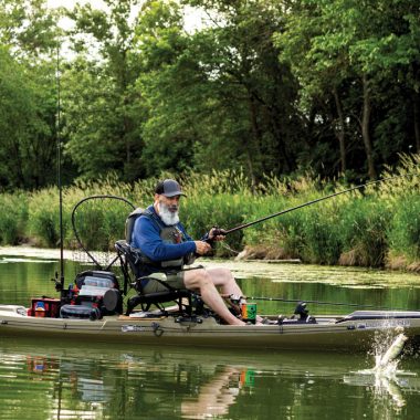 A man reels in a fish from a brown kayak on the water