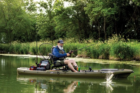 A man reels in a fish from a brown kayak on the water