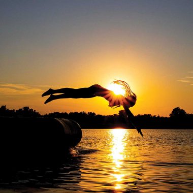 A girl dives off of a floating tube into the water at sunset.