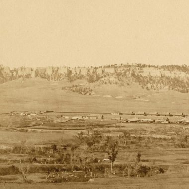 A historical sepia-toned photograph of tents set up small against a backdrop of buttes