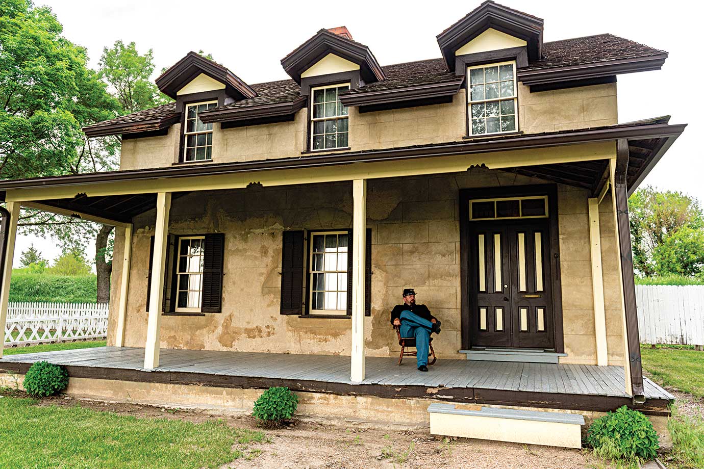 A reenactor in Union blues sits on the porch of a historic home 