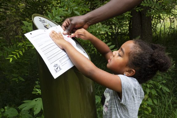 A young girl creates a rub at a Great Park Pursuit post.