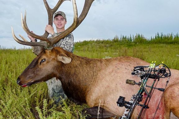 A 21-year-old male archery hunter poses with a male elk that he shot.