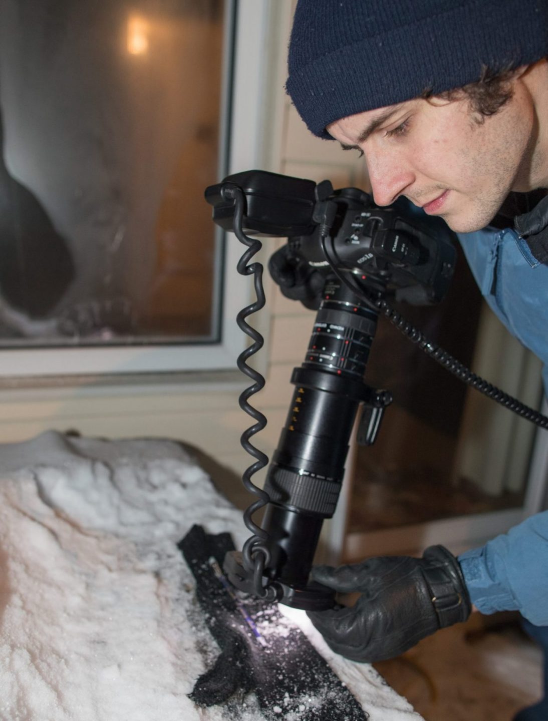 A man practicing macro photography of snowflakes that land on a black glove.