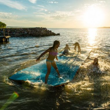 Kids play on a floating mat in a lake.