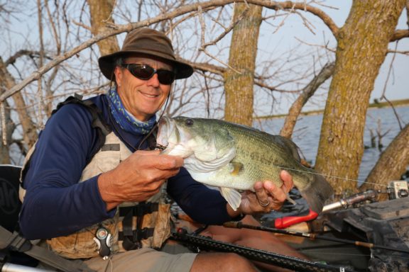 A man holds a large bass he caught while kayak fishing during summer.