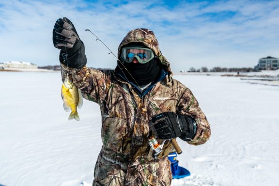 A man ice fishing and holding up a bluegill.