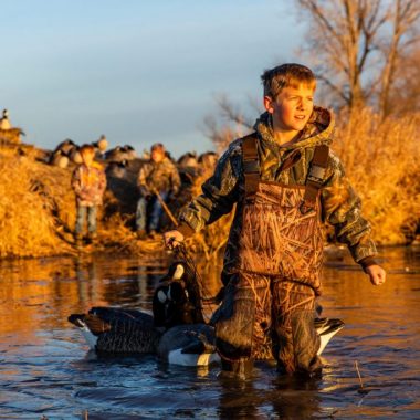 A boy wads in shallow water and holds goose decoys while goose hunting.