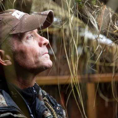 A man inside a waterfowl hunting blind looking out.