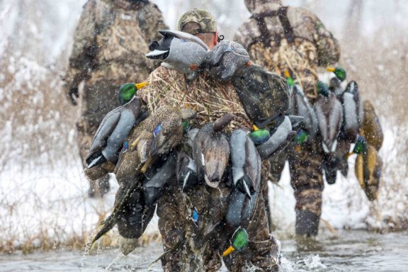 Waterfowl hunters crossing water in winter during snowfall.