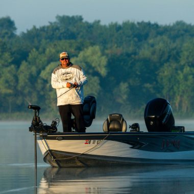 A man stands in a fishing boat, reeling in his line