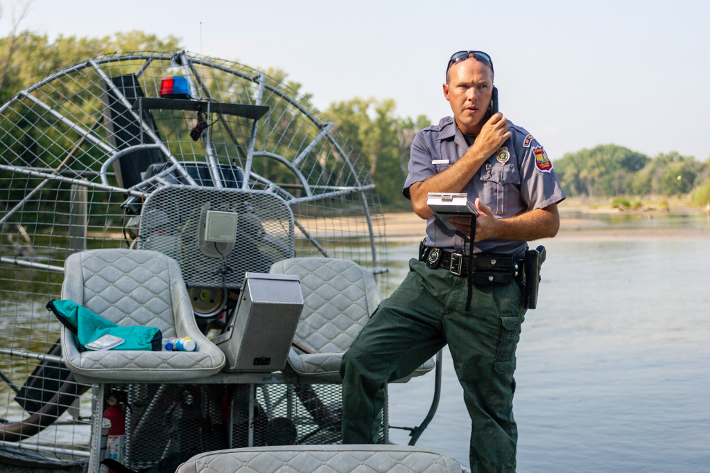 A male conservation officer makes a call to background check two men on the river.