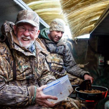 Two men cooking breakfast in a pit duck blind.