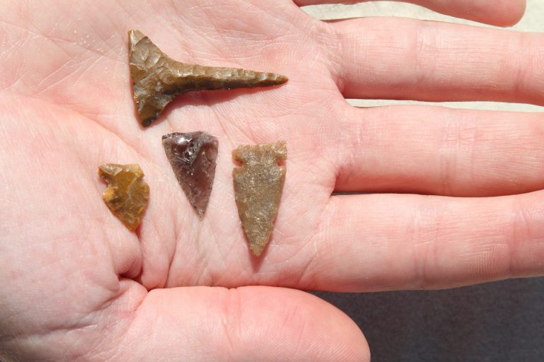 A hand holds three stone arrow points made long ago.