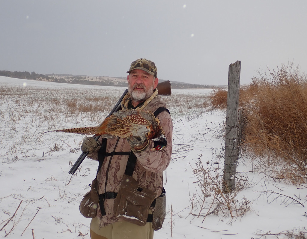 Daryl Bauer holding a pheasant while hunting in snow.