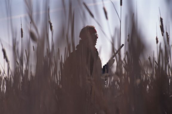 A silhouetted upland hunter walks through tallgrass prairie.