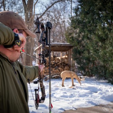 A man aims at a foam deer with a bow while practicing archery hunting.