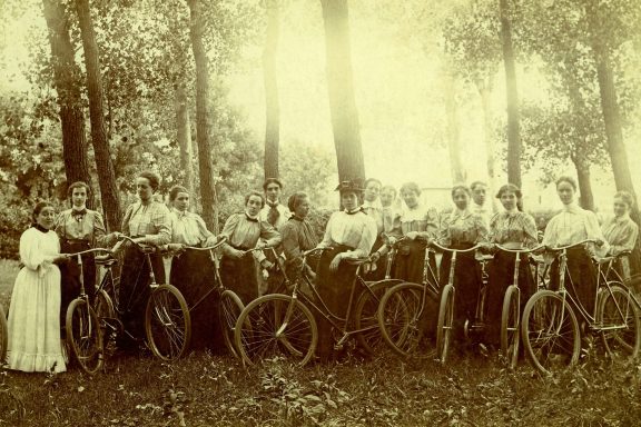 A group of women pose with their bicycles in a forested Nebraska area in 1895.