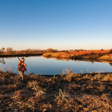 Older man hunting quail by a lake.