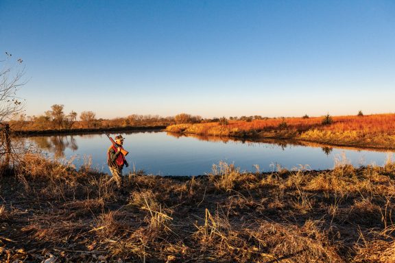 Older man hunting quail by a lake.