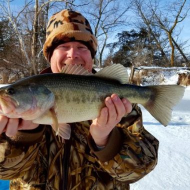 A man holds up a largemouth bass caught while ice fishing in Nebraska.