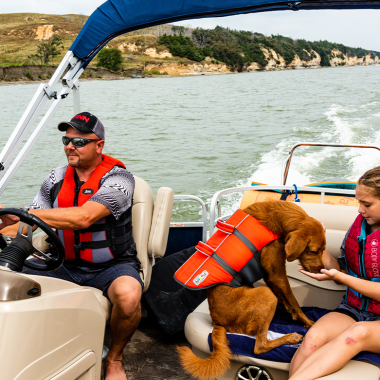 A family and their dog boating on a lake wearing life jackets.