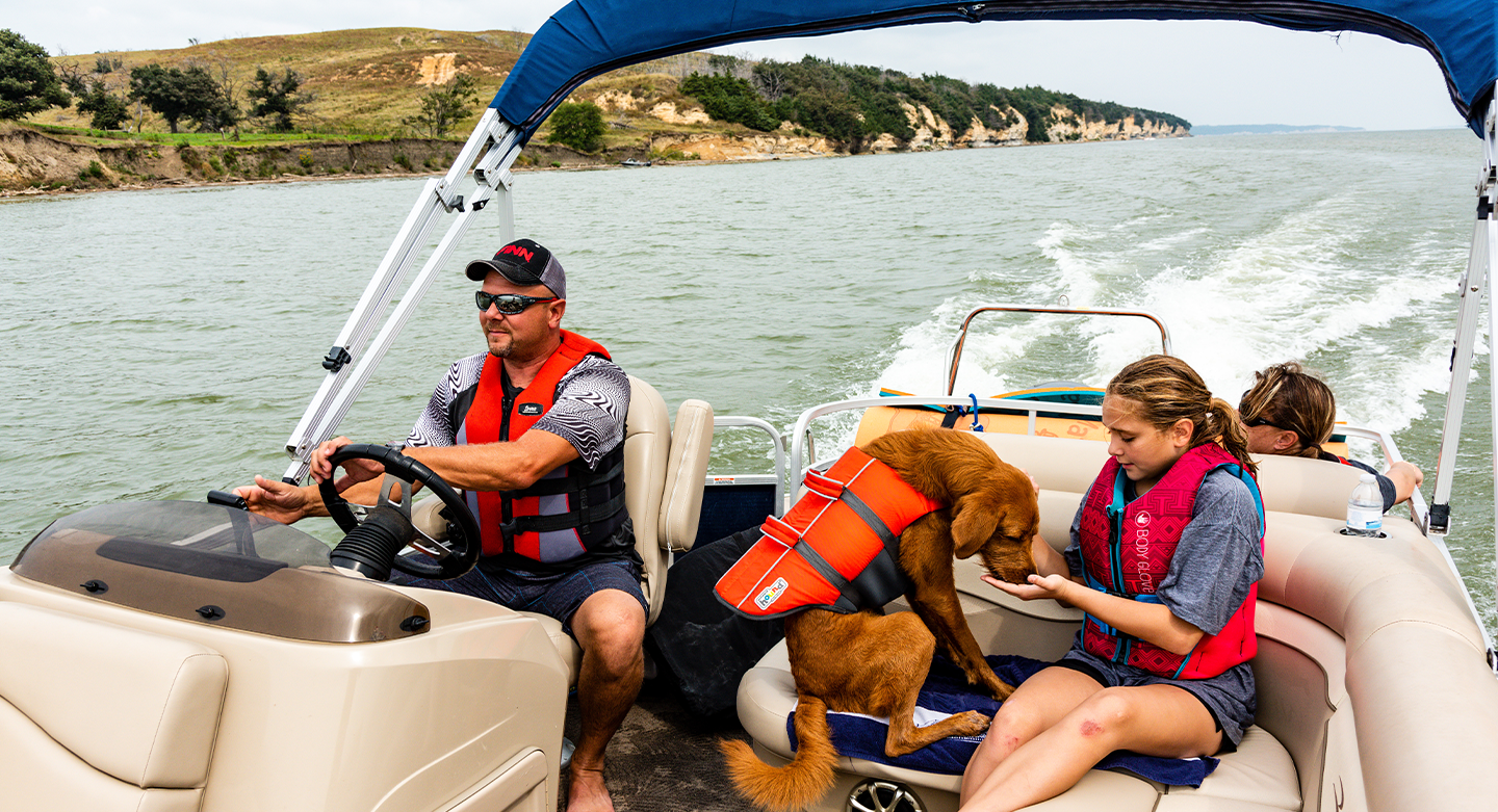 A family and their dog boating on a lake wearing life jackets.