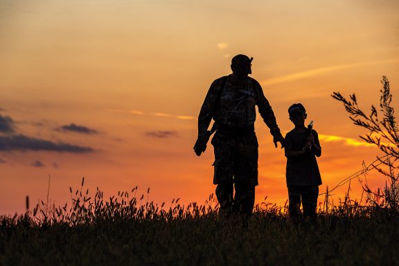 Silhouette of an adult hunter mentoring a kid.