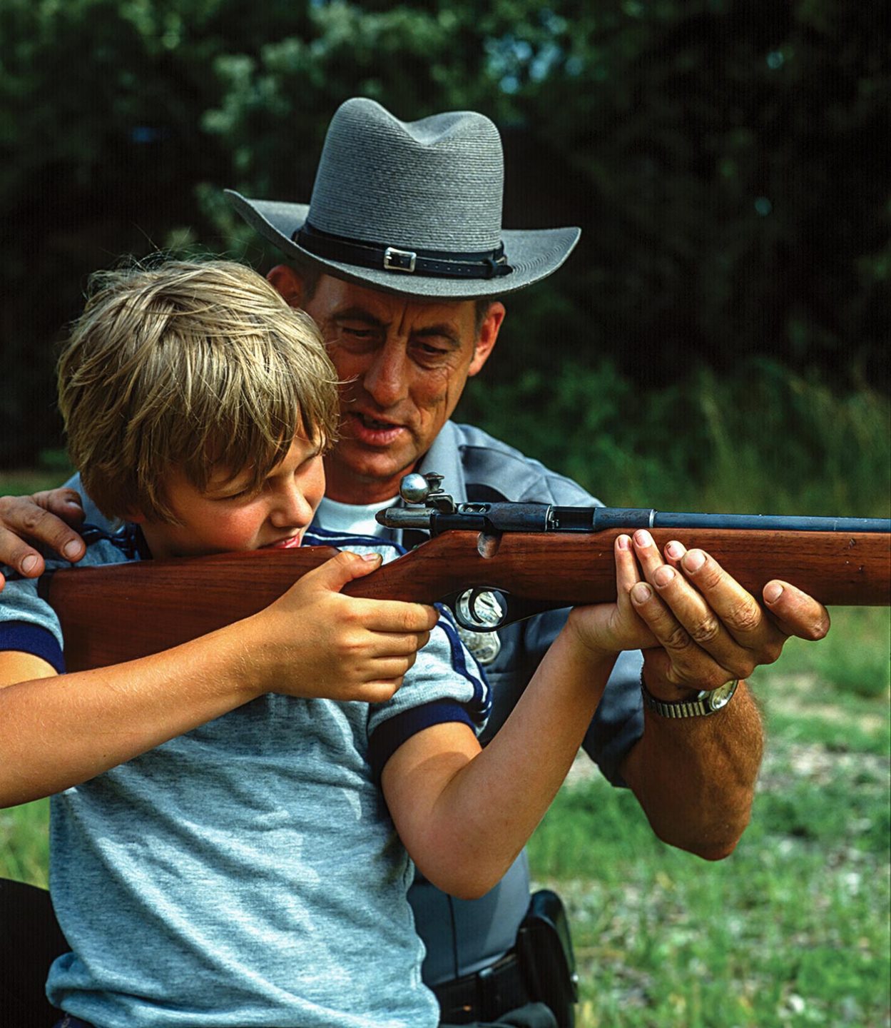 A conservation officer teaching a young boy how to shoot a rifle.