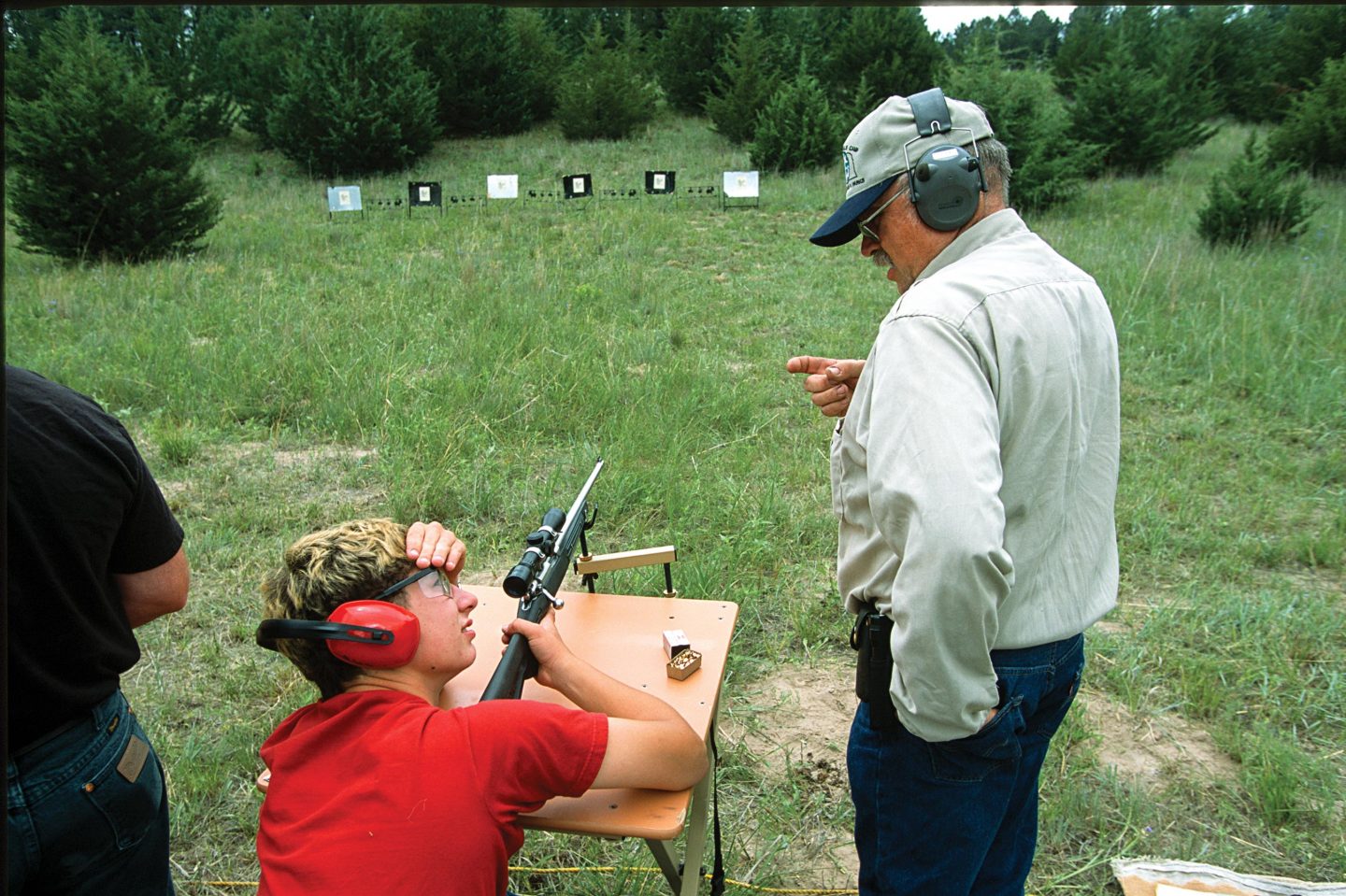 A male shooting instructor teaching a young boy how to shoot at the range.