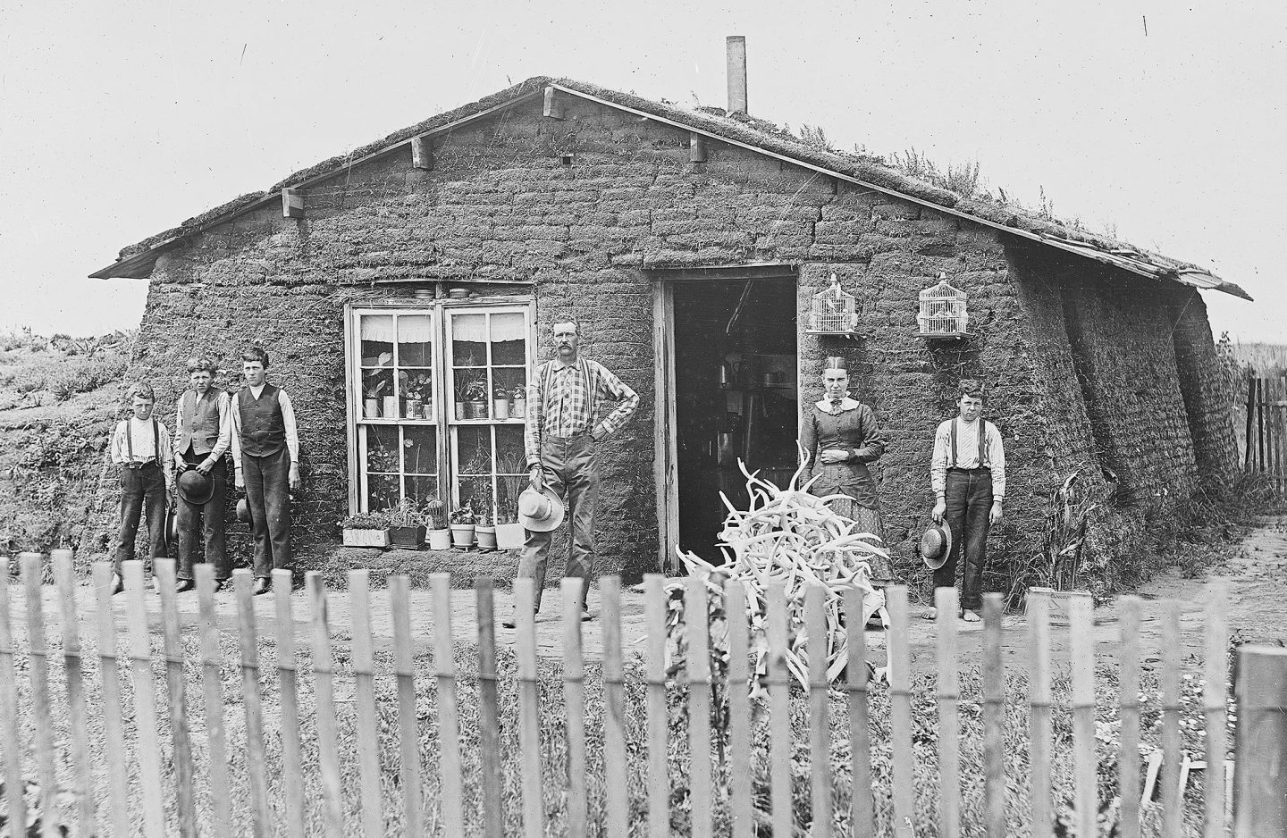 A family in front of a sod house that is fenced in.