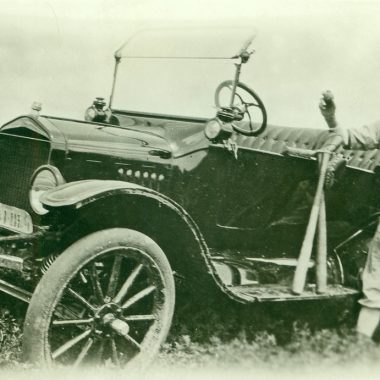 A man stands next to his car that is parks on the hill of a ditch