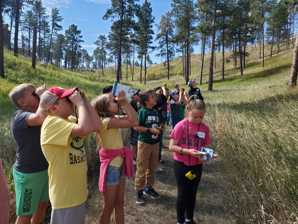 Children with binoculars to their eyes look up into the trees 