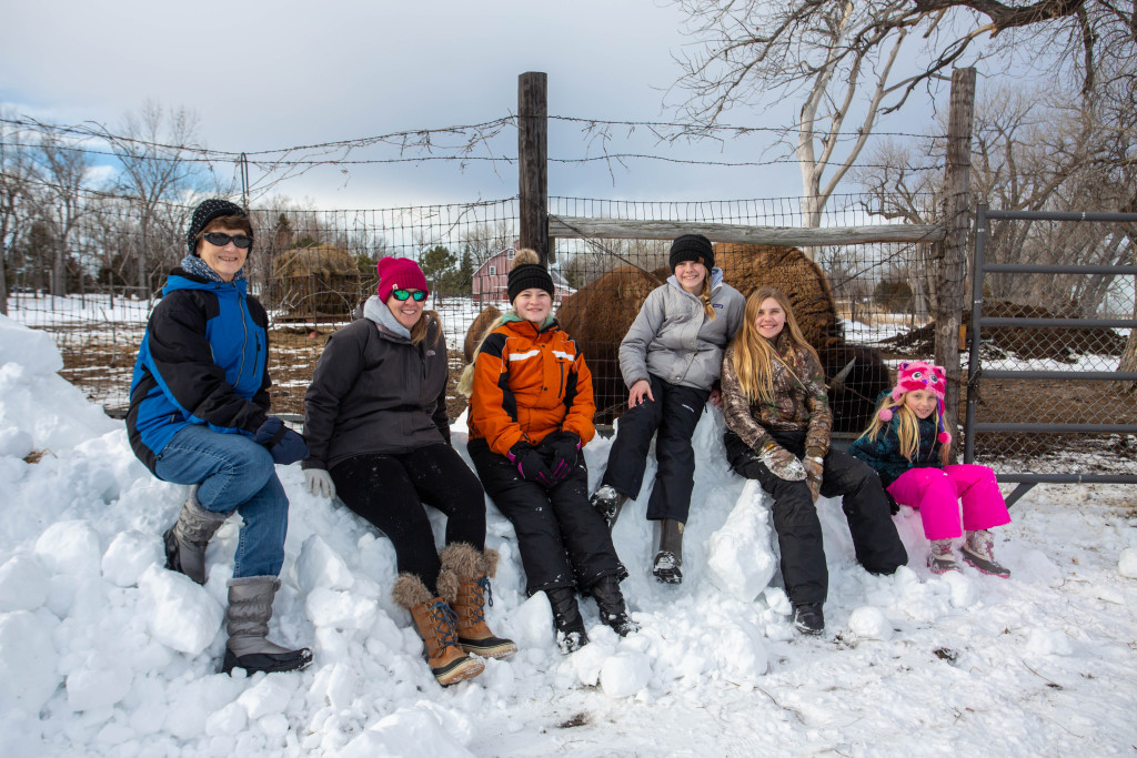 a group of people in winter gear sit on a snowbank for a photo