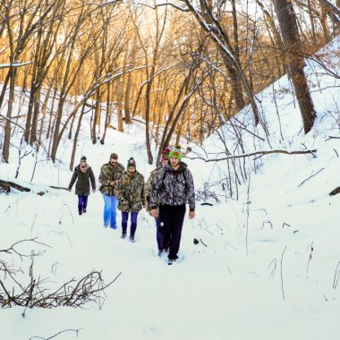 A group of five men and women hike through snow