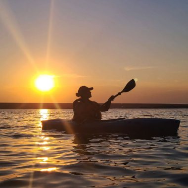 A woman kayaks at sunset on a lake.